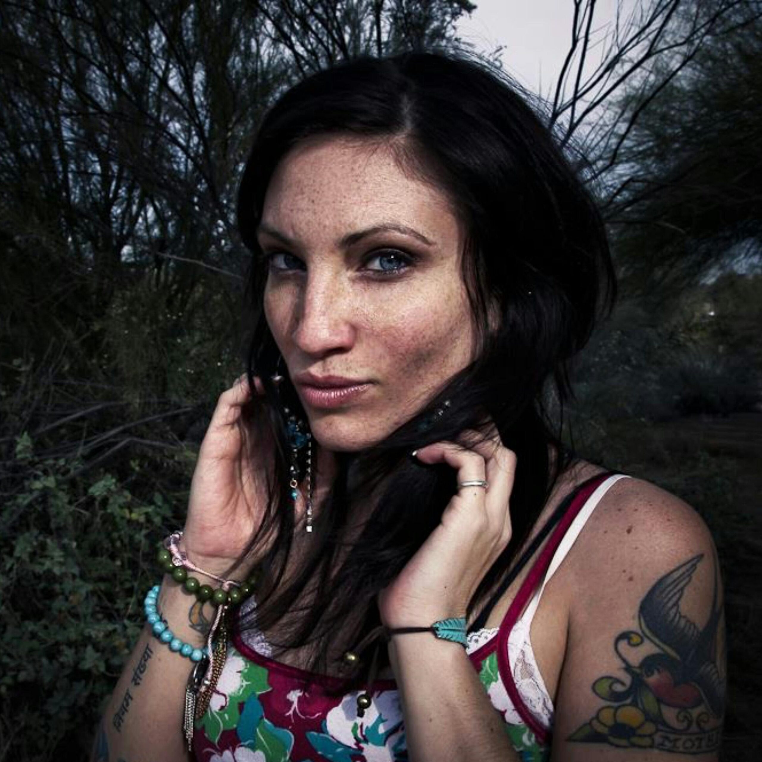 A striking portrait of a woman with tattoos surrounded by nature, highlighting her beauty.