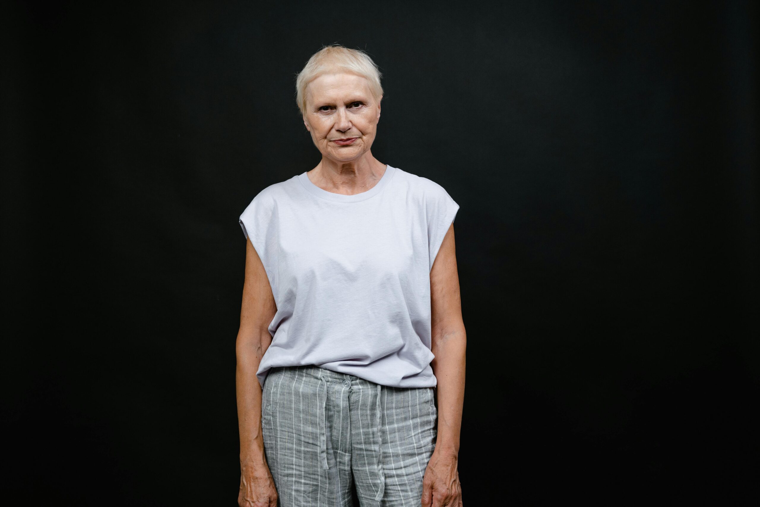 Portrait of a senior woman in a casual outfit against a black background, capturing individuality and expression.